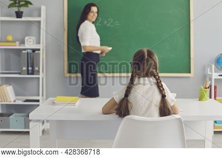 Schoolkid Sitting At Desk And Listening Attentively To Teacher In Modern Classroom