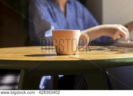 Coffee Cup On Wooden Table In Modern Cafe With Sunlight. Tea Mug On Wood Desk In Coffee Shop And Blu