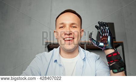 Experienced disabled company worker man waves artificial high tech hand prothesis and smiles at video conference close view