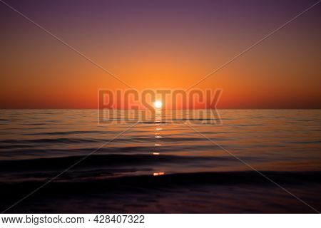 Distant Sun Setting In Clear Skies Over A Calm And Serene Ocean Of Perfection