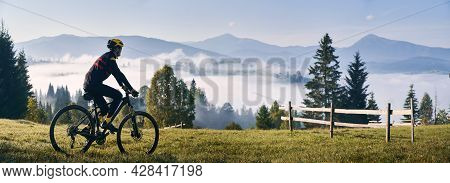 Man Riding Bicycle On Grassy Hill And Looking At Beautiful Misty Mountains. Male Bicyclist Enjoying 
