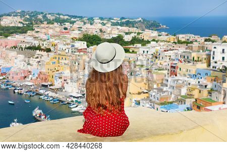 Travels In Italy. Back View Of Beautiful Girl With Hat Sitting On Wall Looking At Stunning Panoramic