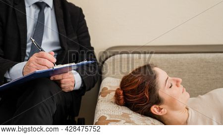 Caucasian Woman Lies On A Couch At A Reception With A Psychotherapist. An Elderly Man Works As A Psy