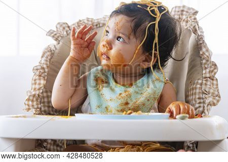 Adorable Little Child Funny Girl Eating Spaghetti With Spoon While Sitting In High-powered Chair At 