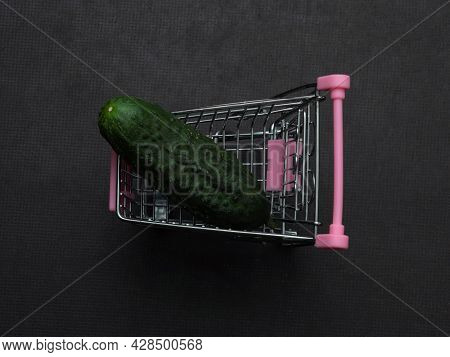 One Green Cucumber Is Lying In A Small Shopping Trolley. A Farmer's Vegetable In A Toy Metal Cart.