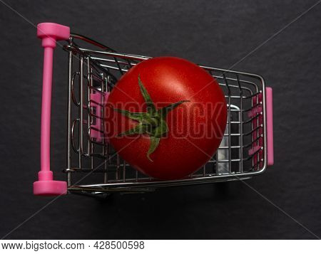 One Red Tomato Is Lying In A Small Shopping Trolley. A Farmer's Vegetable In A Toy Metal Cart.