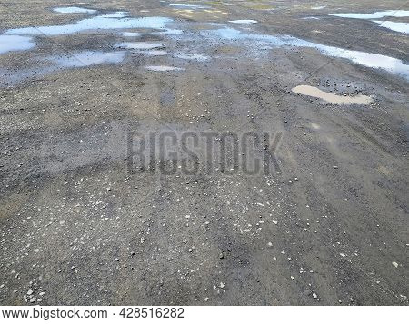 Gravel Road Background With Puddles Of Mud And Rain Water. Abstract Textures. Puddles Of Dirty Water