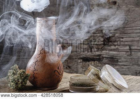 Old Brown Steamung Bong And Open Cannabis Grinder With Chopped Marijuana Weed And Medical Cannabis B
