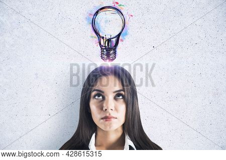 Portrait Of Thougtful Young European Businesswoman With Creative Light Bulb Sketch On Concrete Wall 