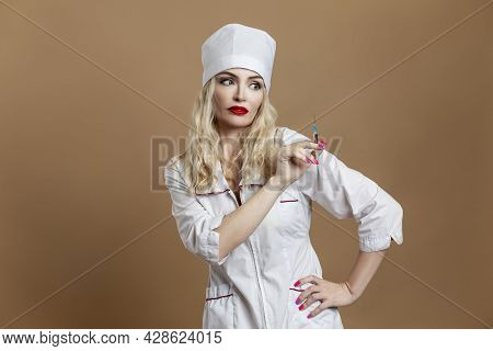 A Beautiful Young Woman In The Uniform Of A Nurse With A Syringe In Her Hand. Sexy Blonde With Red L