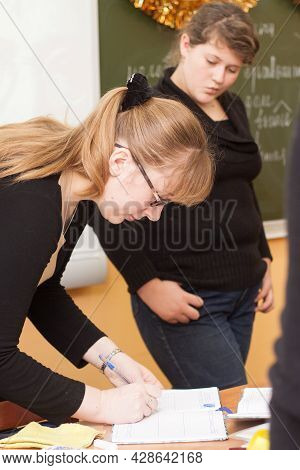 Tula, Russia - January 18, 2013: Beautiful Young Teacher Woman Writing In Exsercise Book While Girl 