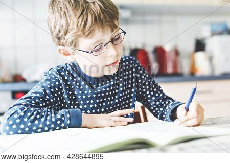 Cute Little Kid Boy With Glasses At Home Making Homework, Writing Letters With Colorful Pens. Little