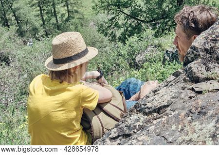 Father And Son Sit On A Stone High In The Mountains And Admire The Beautiful Nature. Back View. Calm