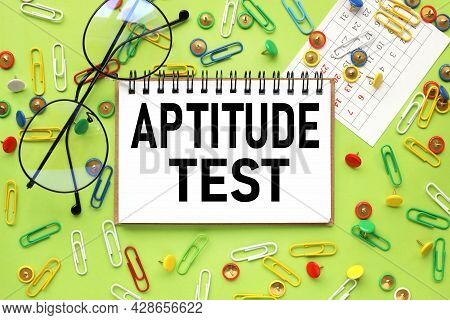 Aptitude Test, Text On Sticker On Bright Green Background. Near Paper Clips And Buttons