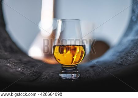 A glass of whiskey in old oak barrel. Copper alambic on background. Traditional alcohol distillery concept