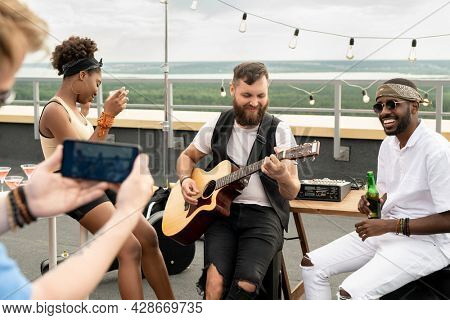 Multracial friends with drinks enjoying rooftop party while one of them shooting video