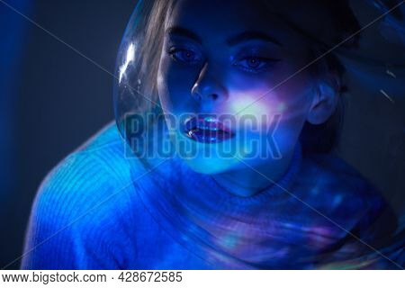 Beautiful tender girl with blue eyes in a glass spacesuit looks at camera against the background of outer space. Space concept. Copy space. 