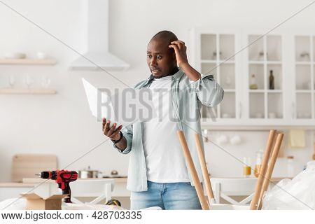 Confused Black Man Having Hard Time Assembling Furniture And Reading Self-assembly Manual In Kitchen