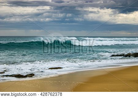 Turquoise Wave Crashing On Beach Set Against An Angry Stormy Sky