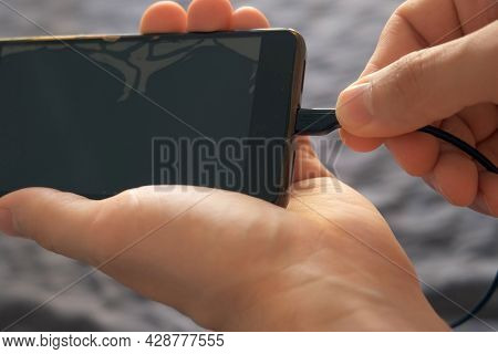 Man Inserts A Cable Into A Mobile Phone For Charging, Hands Closeup View. Inserting A Charger Into A