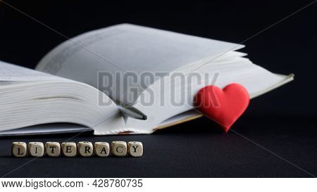 Lettering Literacy Next To An Open Book, Red Heart And Pen. The Concept Of Sympathy For Literacy And
