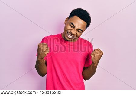 Young african american man wearing casua t shirt very happy and excited doing winner gesture with arms raised, smiling and screaming for success. celebration concept. 