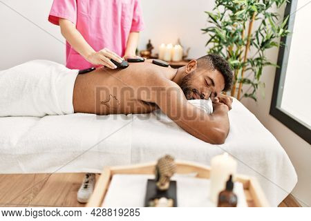 Man reciving back massage with black stones at beauty center.
