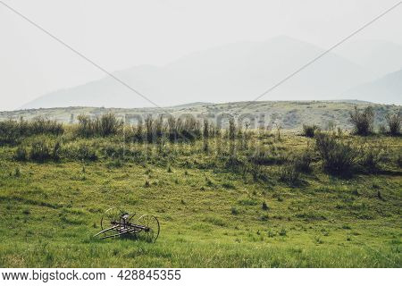 Scenic Green Landscape With Old Altaic Horse Plow With Saddle Among Lush Grasses On Background Of Mo