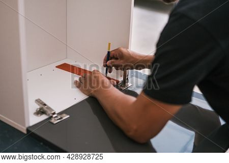 Hands Of A Man Marking A Line On A Piece Of Wood Of A Kitchen He Is Assembling