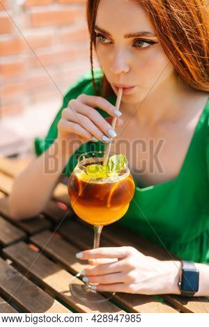 Close-up Face Of Attractive Young Woman Drinking Cocktail Through Straw Sitting At Table In Outdoor 