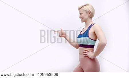 Sporty Girl Dressed In Activewear Posing For The Camera. Side View. Pointing At A Side With Her Fing