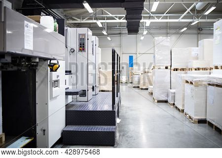Printing Shop Or Factory Interior With Modern Offset Paper Machine And Piles Of Sheets In Background