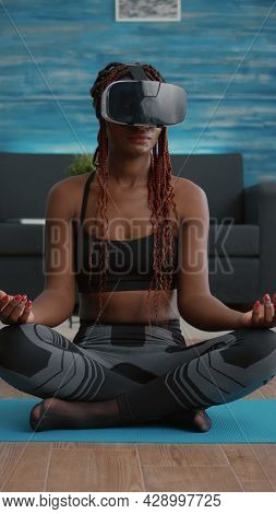 Fit Black Woman Wearing Virtual Reality Headset While Sitting On Yoga Map In Lotus Position During M