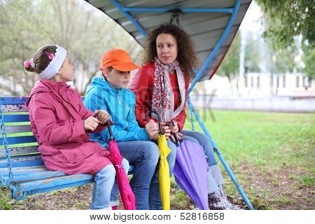 A mother and two children with umbrellas sitting on a swing