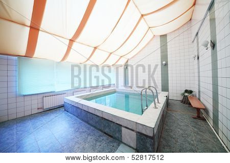 A small indoor pool with tiles on walls and floor and blinds on the windows