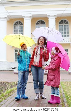 Mother with two children stand with colorful umbrellas on a cloudy day on the street