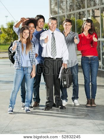 Full length portrait of confident college students and professor gesturing thumbsup on campus