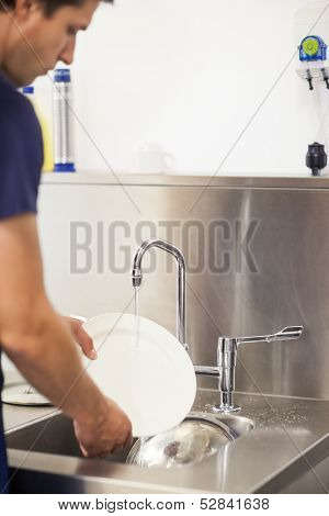 Kitchen porter cleaning plates in sink in professional kitchen