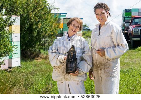 Portrait of happy female beekeepers with smoker standing at apiary