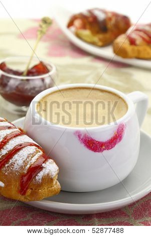 Cup of coffee with lipstick mark and croissant with strawberry jam