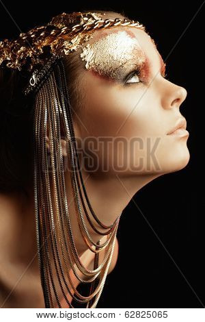Art project: beautiful woman with golden make-up. Jewelry, make-up. Fashion. Over black background.