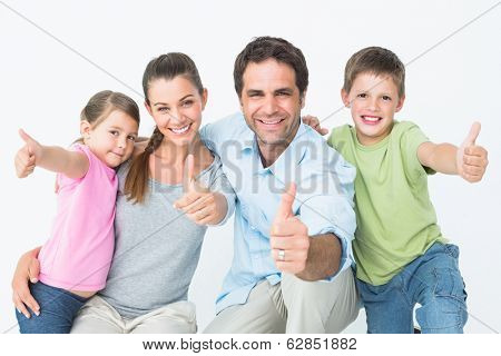 Cute family smiling at camera together showing thumbs up on white background