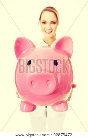 Young beautiful female doctor holding a piggybank.