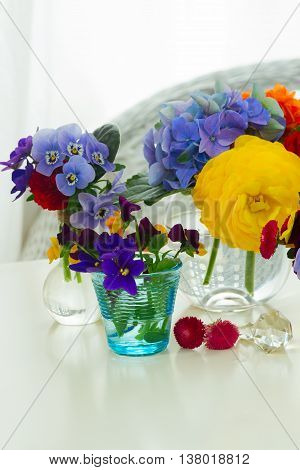 Colorful violets and pancies cut flowers in vases on white desktop