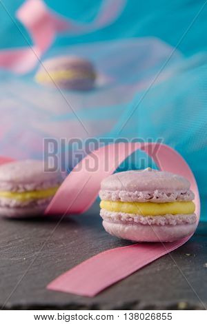 Homemade delicious appetizing sweet lavender macaroons with vanilla creme patissiere in colorful setting with blue teal fabric and pink ribbon