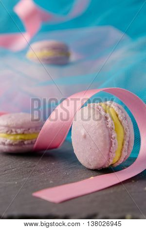 Homemade delicious appetizing sweet lavender macaroons with vanilla creme patissiere in colorful setting with blue teal fabric and pink ribbon