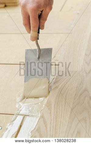 Laying hardwood parquet. Worker puts glue on the floor.