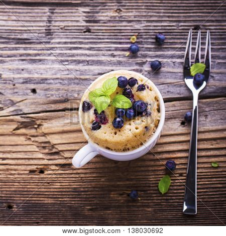 Healthy breakfast. Fresh homemade mug cake with forest blueberries in a white ceramic bowl with a sprig of ripe berries on the gray wooden background. selective focus