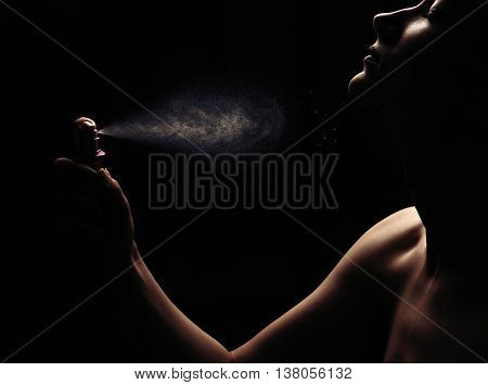 Woman with spraying perfume on black background