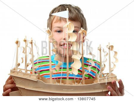 Small boy in striped shirt holds artificial wooden ship with paper sails